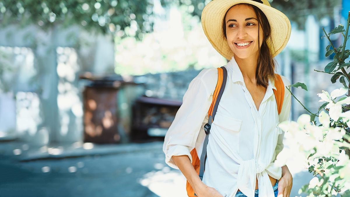 Article Cards Featured Image portrait happy carefree woman tourist in straw hat, white shirt walking and exploring small streets.