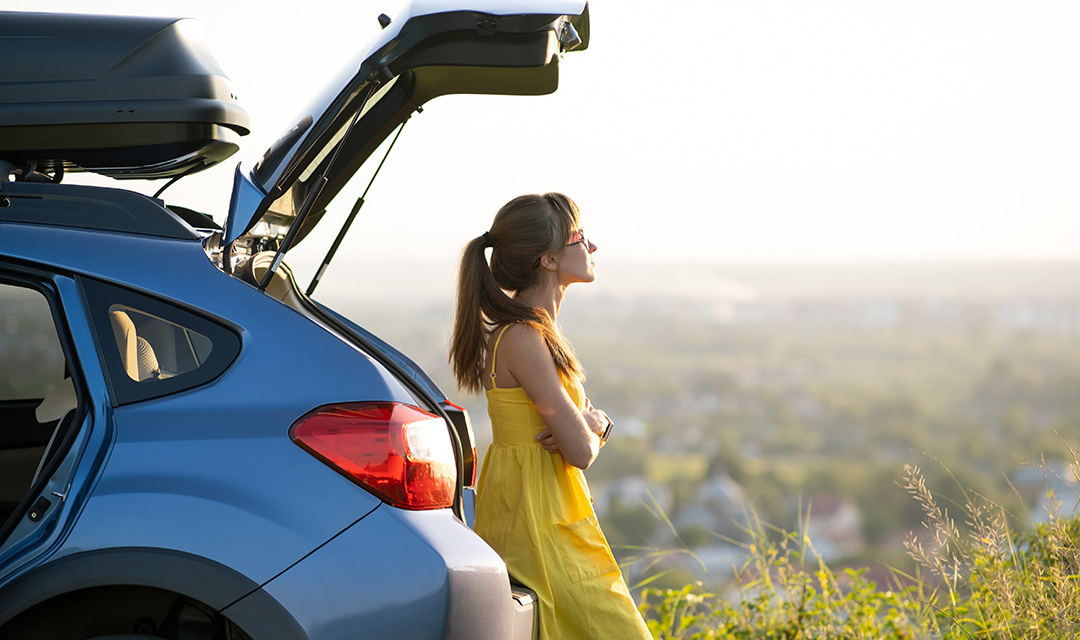 Happy woman driver in summer dress enjoying warm evening near her car. Travel and vacation concept.