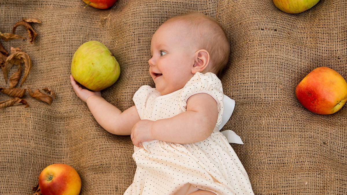 Article Cards Featured Image A baby holds an apple, a popular fruit to celebrate September birthdays.