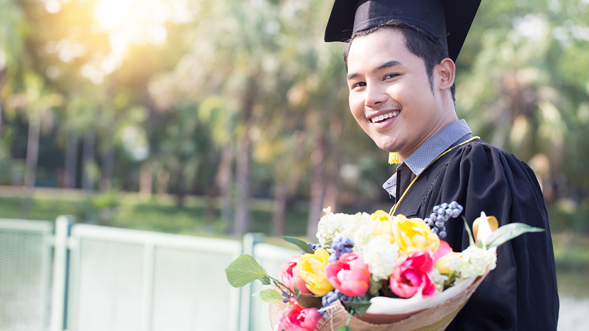 Attractive Asian graduated man in cap and gown smile and holding