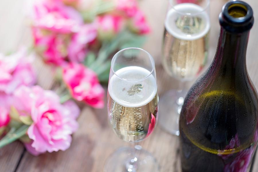 Article Cards Featured Image Bottle of Prosecco and two champagne glasses on a rustic garden picnic table with blossom or flowers in the background. Springtime or Summertime.