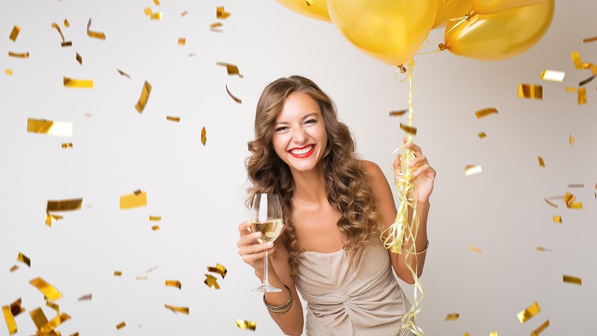 Article Cards Featured Image attractive young stylish woman celebrating new year, drinking champagne holding air balloons, golden confetti flying, smiling happy, white background, isolated, wearing party dress