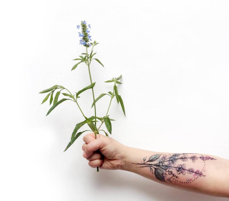 An tattooed with lavender holds a lavender plant. These flowers symbolize devotion, grace, and calmness.