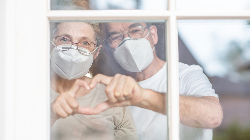 Old couple wearing masks making heart shape with fingers