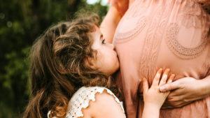 Mommy brain is nature's way of helping moms adjust to motherhood. This photo shows a young girl kissing her mother's belly.