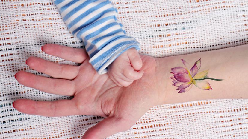 Mother with a lotus flower tattoo holds her baby's hand. Lotus flowers are known for their beauty and grace